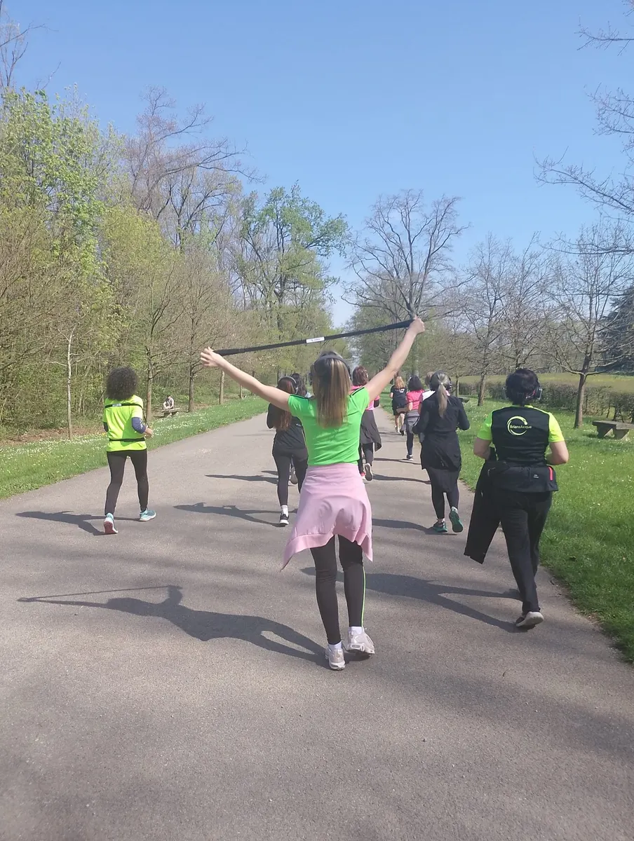 Partecipanti alla camminata metabolica in un viale alberato del parco; una di loro solleva la F-Band sopra la testa