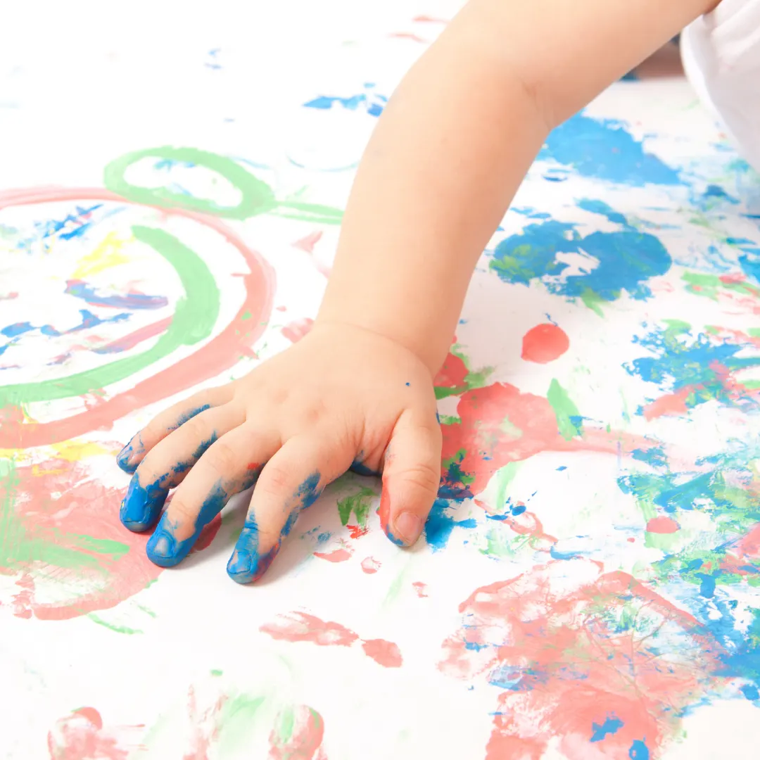 Manina di un bimbo con le dita sporche di colore blu su un foglio dipinto a chiazze