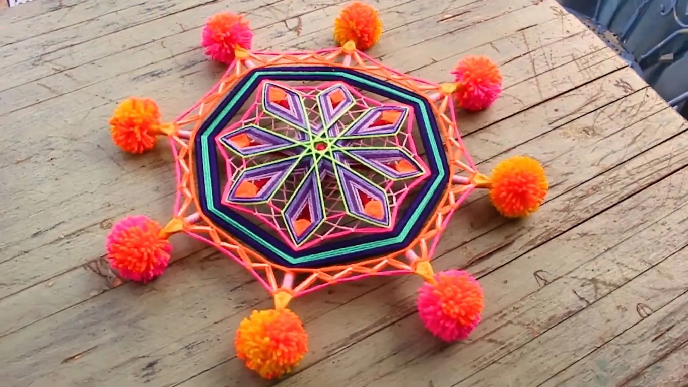 Mandala di lana ottagonale viola e rosa con otto pompon arancioni e fucsia