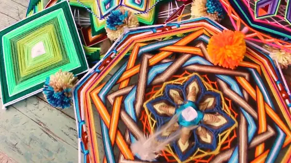 Mandala ottagonale arancione e azzurro con pompon e una piuma, accanto a un rombo di lana verde