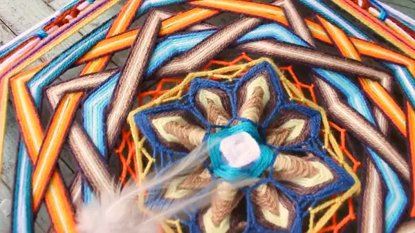 Dettaglio del centro di un mandala: fiore blu e beige con una piuma bianca