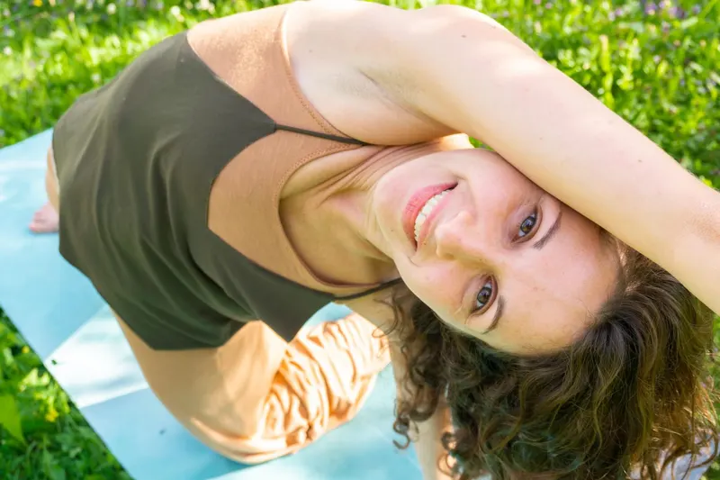 Laura Presicci sorride durante una posizione di yoga su un tappetino nel prato